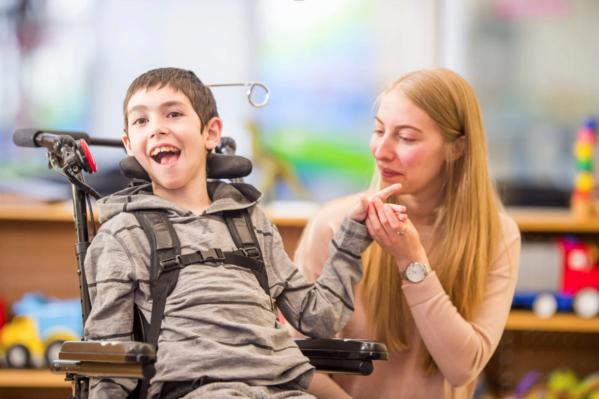 un garçon en fauteuil électrique sourit et une intervenante lui tient la main