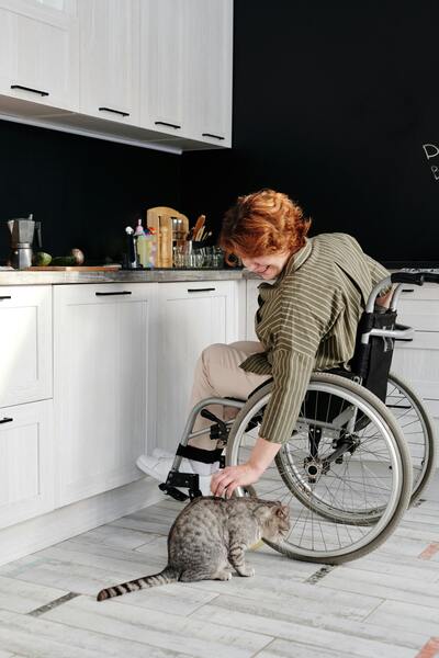 femme dans un fauteuil roulant dans sa cuisine flatte son chat