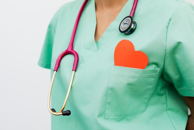 Professionnelle de la santé portant une tenue de couleur verte et un téthoscope ainsi qu'un coeur en carton rouge dans la poche
