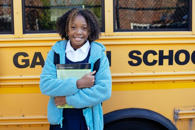 une enfant tenant ses livres dans ses bras devant un autobus scolaire jaune