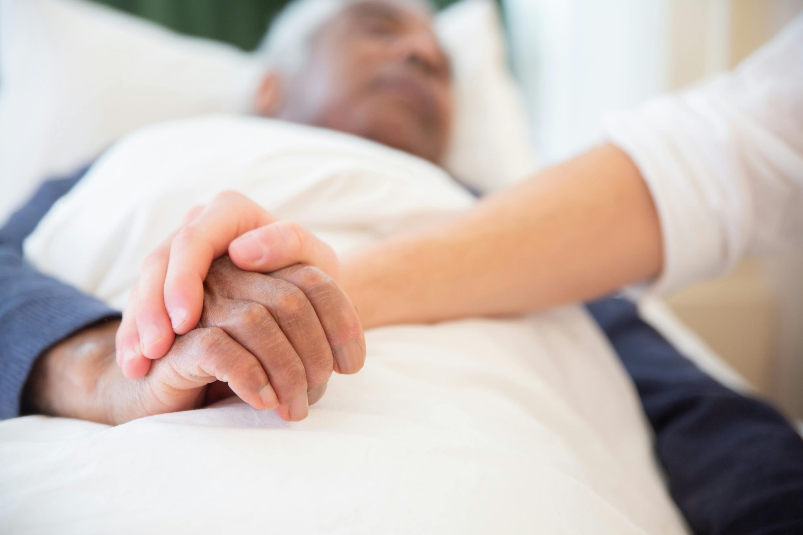 Une personne tient la main d'une personne mourante dans son lit